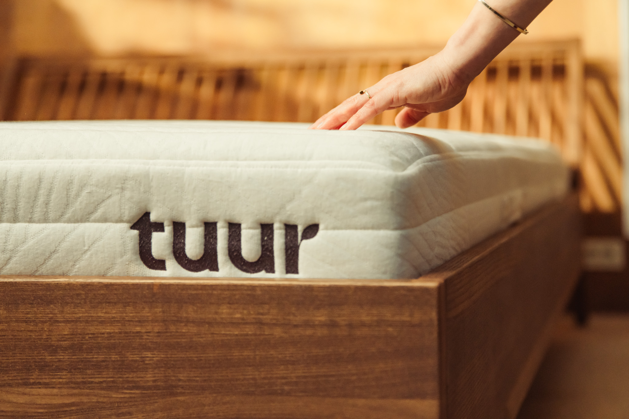 Tuur Original Matras in het Tuur bedkader. Vrouw die zacht met haar hand erover streelt.